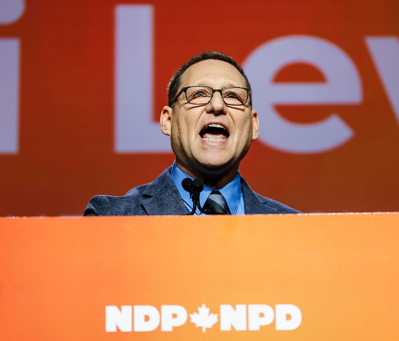 A man in a suit stands on an orange platform.