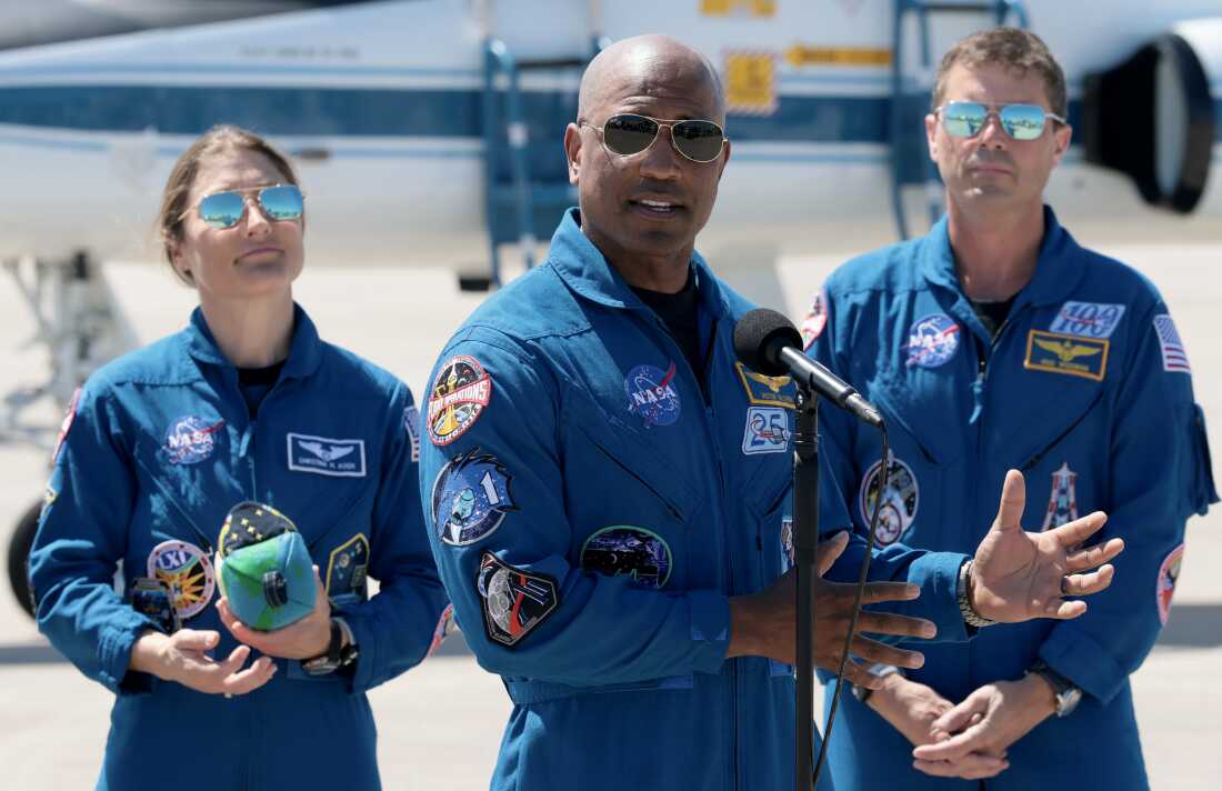 Artemis II crew members - mission specialist Christina Koch (left) and commander Reid Wiseman (right) - listen as pilot Victor Glover speaks to the media after landing at the Kennedy Space Center on March 27, 2026 in Cape Canaveral, Florida. The astronauts' planned 10-day mission will take them around the Moon and back to Earth.