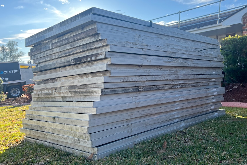 A large pile of solar panels in a silver frame on a piece of green grass.